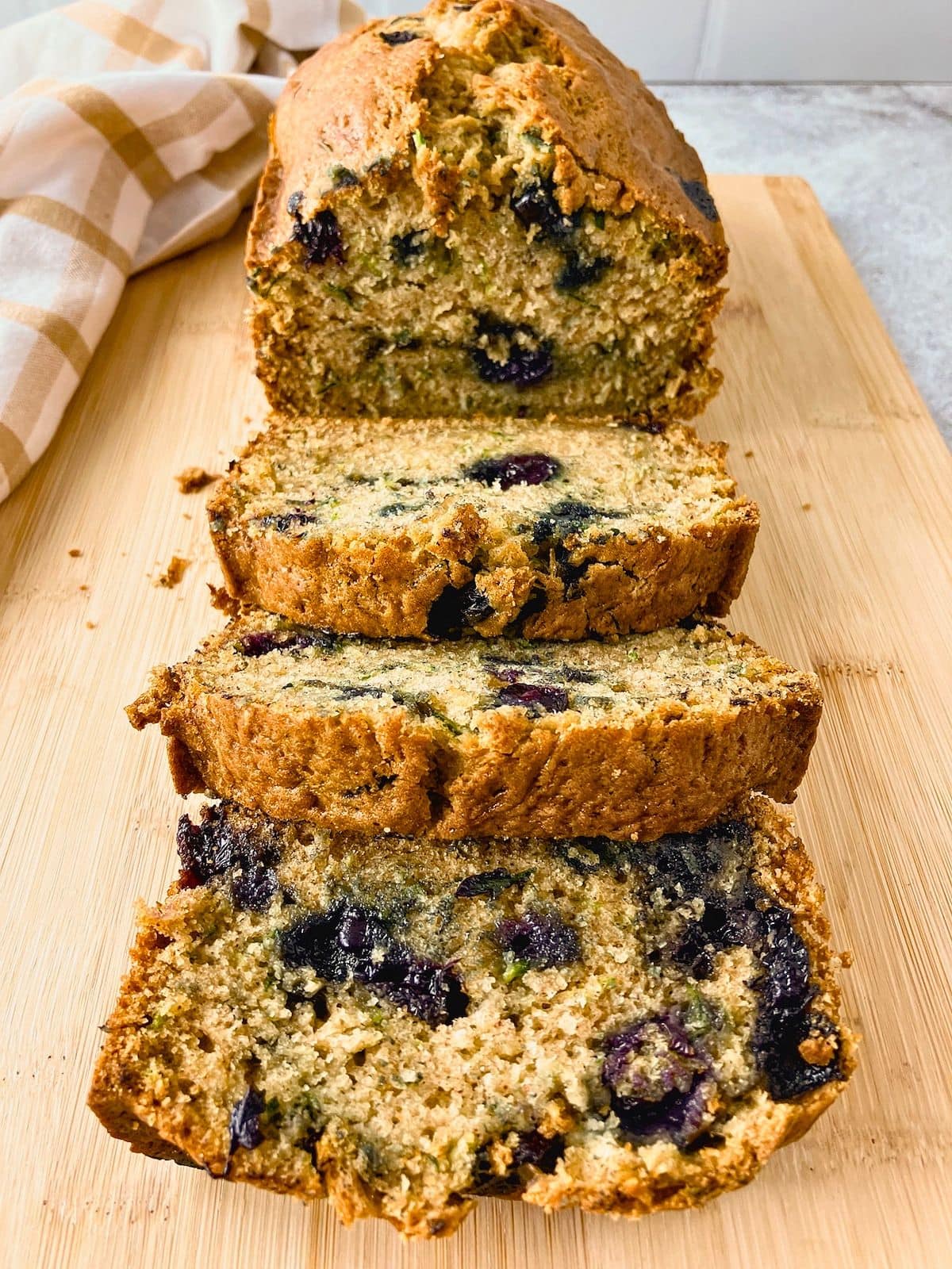 Sliced blueberry zucchini bread arranged on a cutting board with the remaining loaf behind it.