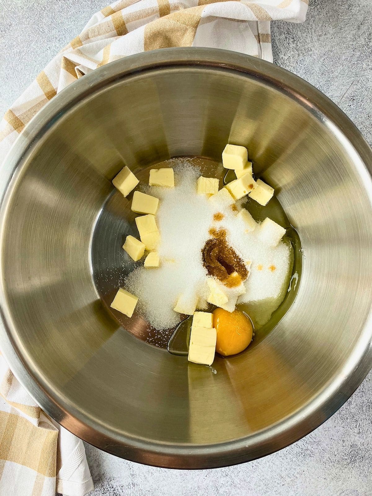 Butter cubes, sugar, egg, and vanilla in a stainless steel mixing bowl.
