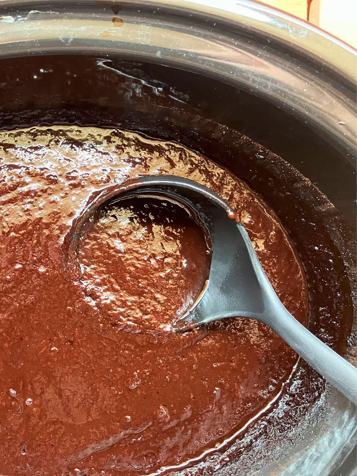 Thick slow cooker plum butter being stirred in the slow cooker with a ladle. The plum butter has cooked down to a smooth, glossy consistency.