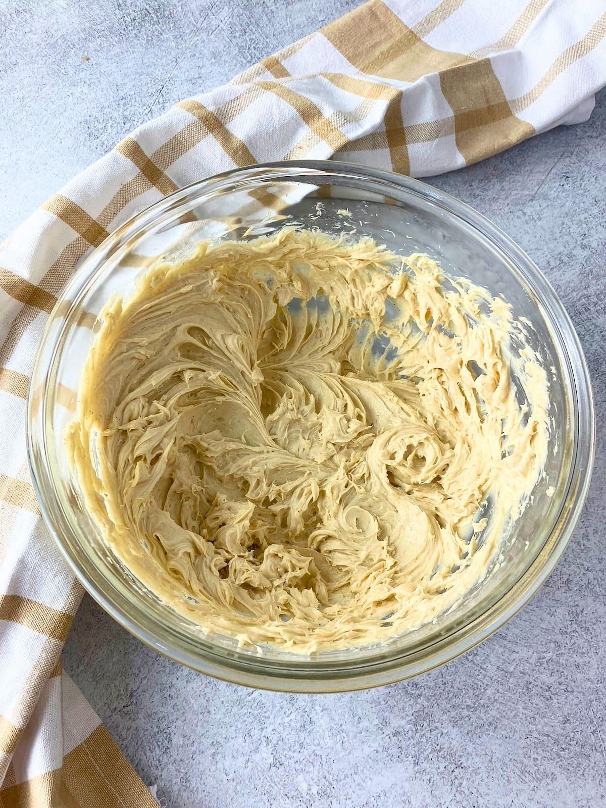 Overhead view of finished cream cheese apple dip, whipped until light and fluffy, in a clear glass mixing bowl. The smooth creamy dip is ready to transfer to a serving bowl with sliced apples.