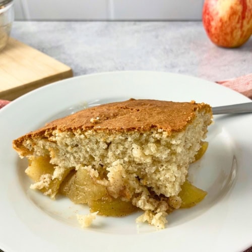 Slice of golden brown apple cobbler on a white plate with tender cinnamon apples peeking out beneath the soft cake topping. This finished serving shows what the easy apple cobbler recipe looks like after baking.