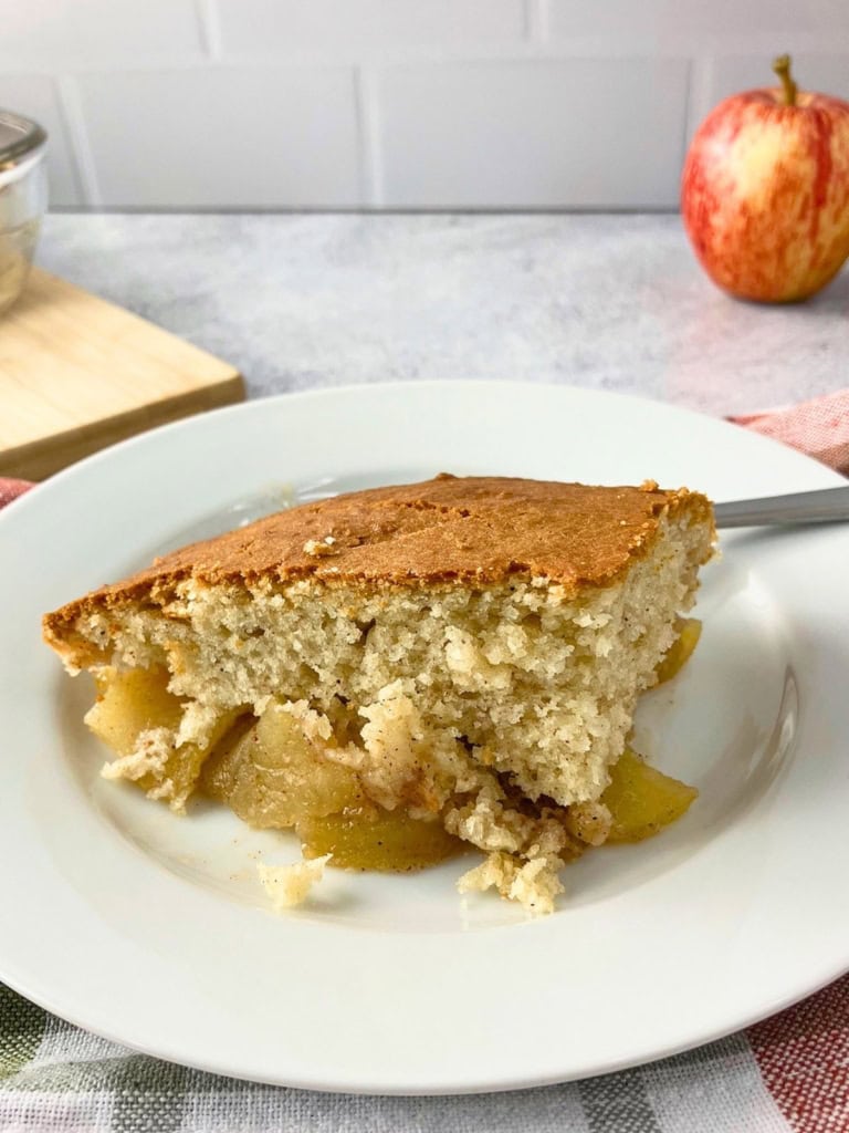 Slice of golden brown apple cobbler on a white plate with tender cinnamon apples peeking out beneath the soft cake topping. This finished serving shows what the easy apple cobbler recipe looks like after baking.