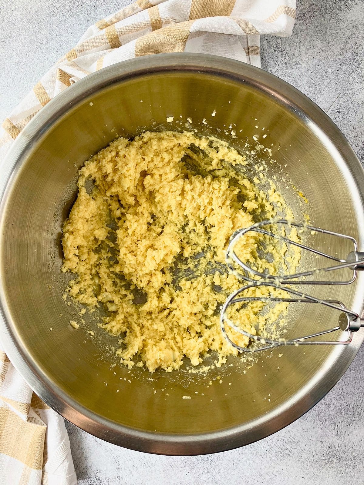 Butter and sugar mixture creamed in a stainless steel bowl with hand mixer beaters resting over top.