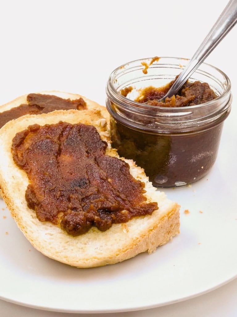 Homemade apple butter in a jar and spread on two slices of bread.