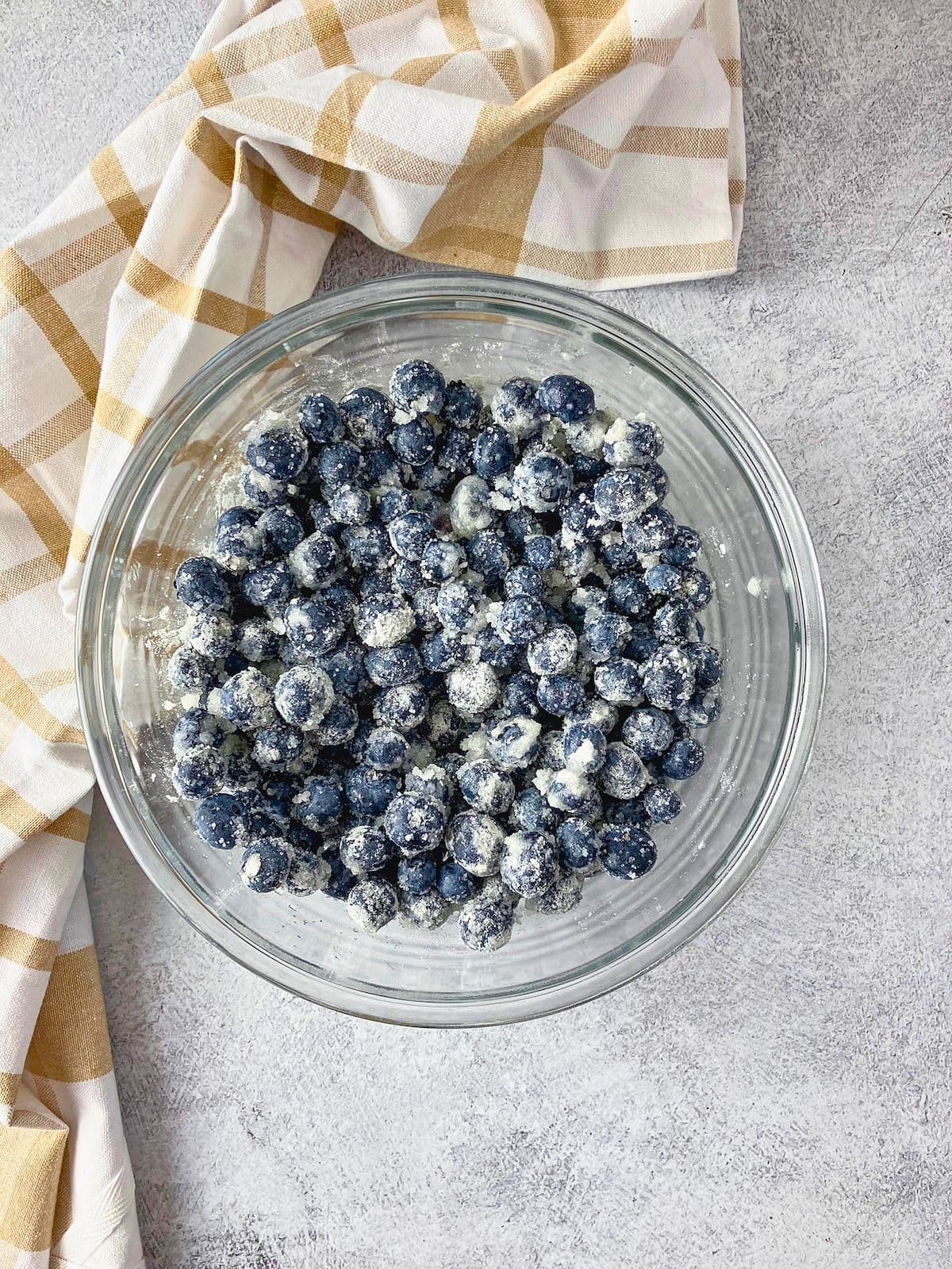 Blueberries tossed with sugar, lemon juice, and flour in a glass bowl for the blueberry cobbler filling.