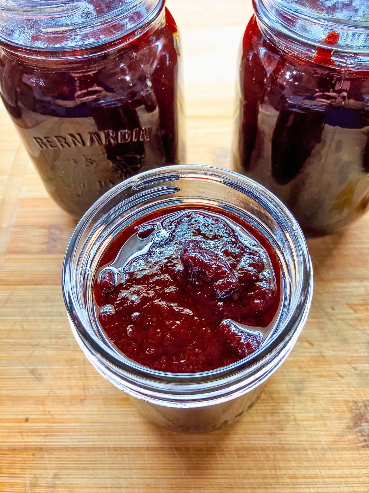 Open jar filled with thick dark red slow cooker plum butter with two larger jars of plum butter in the background.