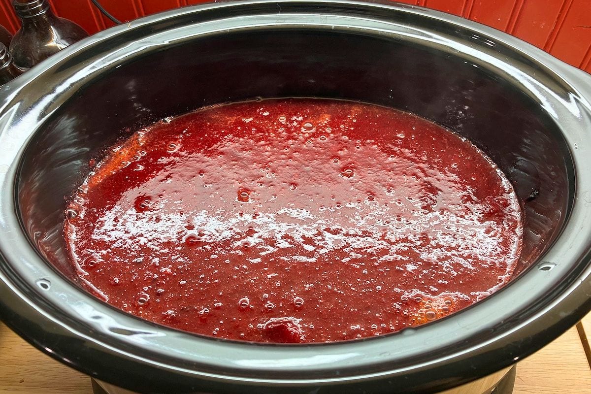 Smooth red plum puree filling a slow cooker after the cooked plums have been blended. This stage of slow cooker plum butter is ready to continue cooking until thickened.