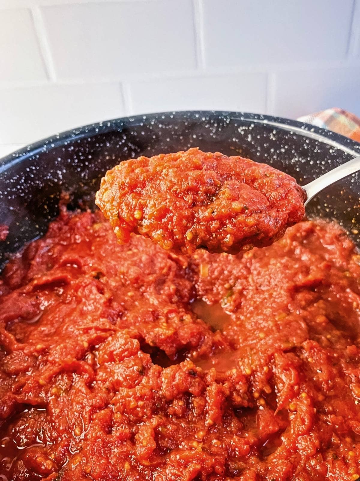 A spoonful of thick roasted tomato sauce is held above a roasting pan filled with the finished chunky sauce.