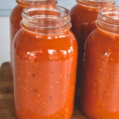 Four open mason jars filled with roasted tomato sauce on a wooden surface.