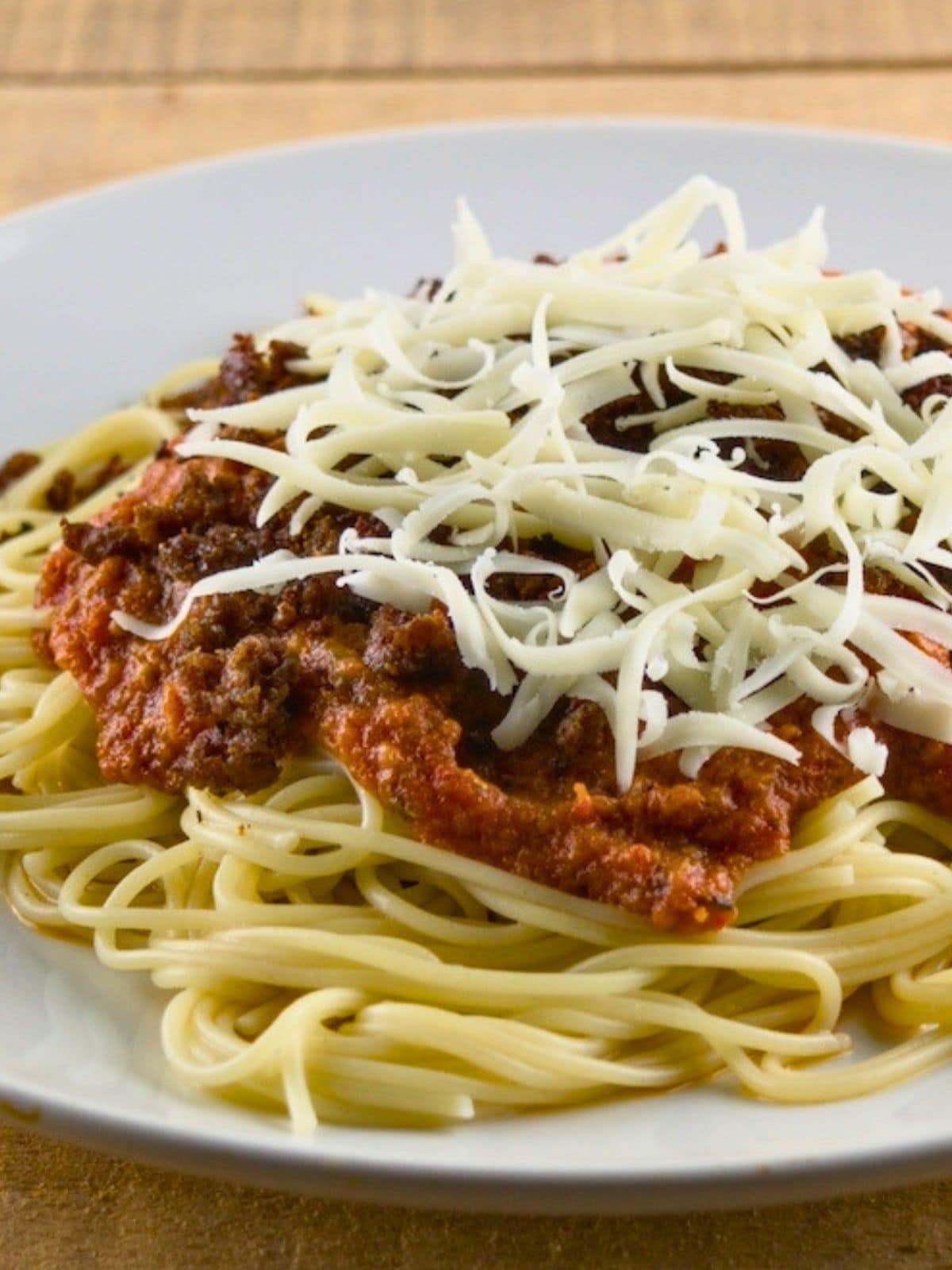 Spaghetti topped with chunky roasted tomato sauce and shredded cheese on a white plate.