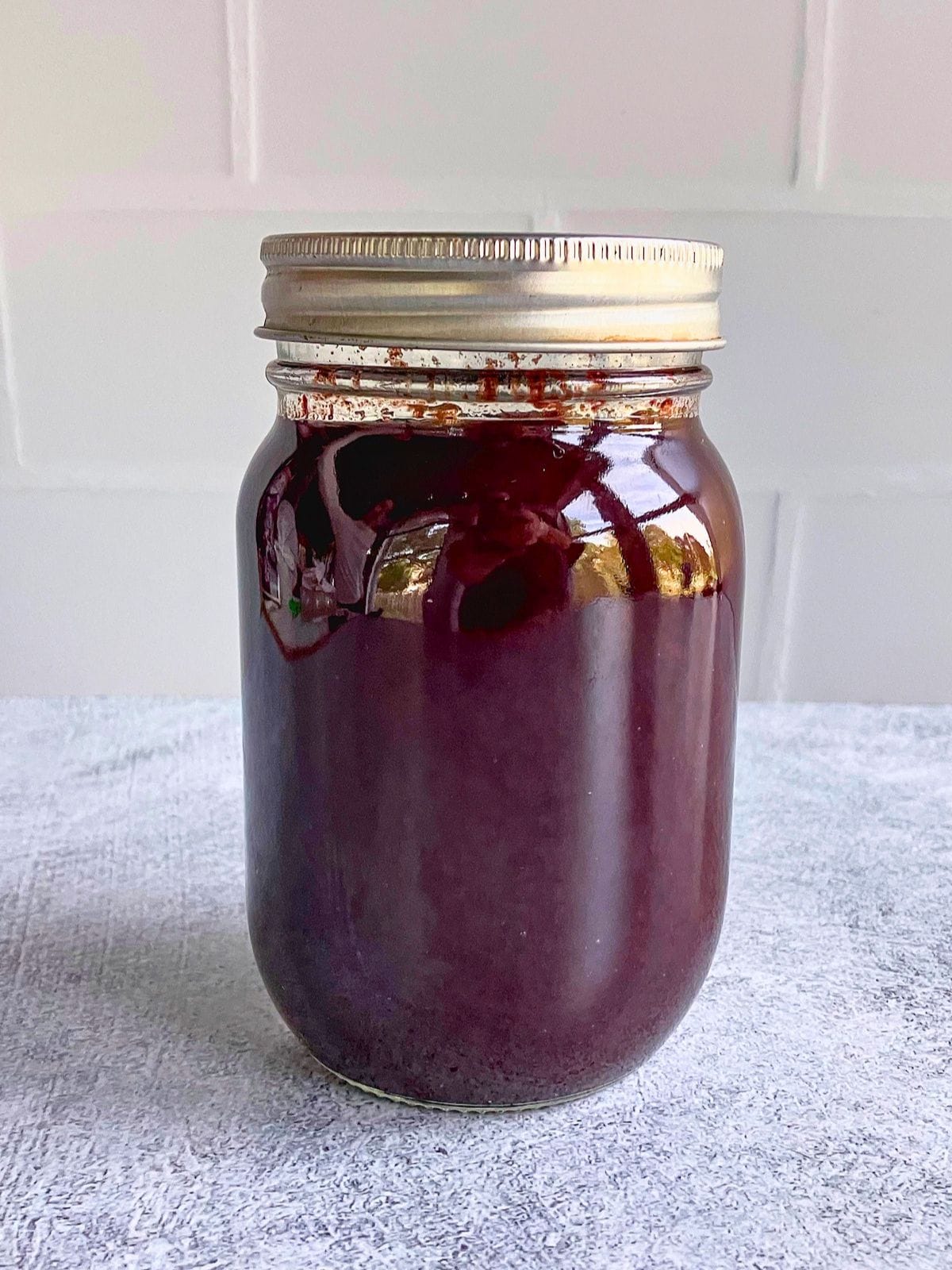 Sealed mason jar filled with dark red slow cooker plum butter on a gray counter.