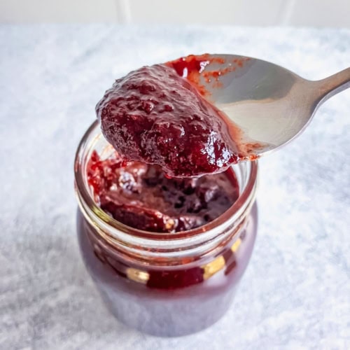 Close-up of slow cooker plum butter on a spoon above an open jar of plum butter.