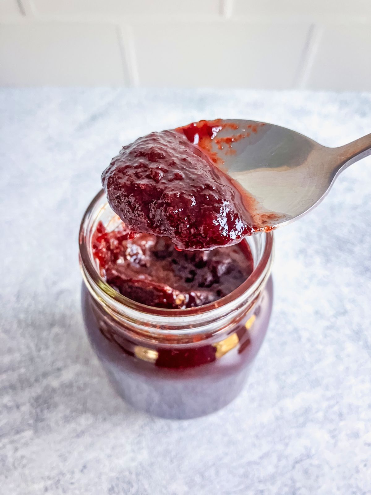 Close-up of slow cooker plum butter on a spoon above an open jar of plum butter.