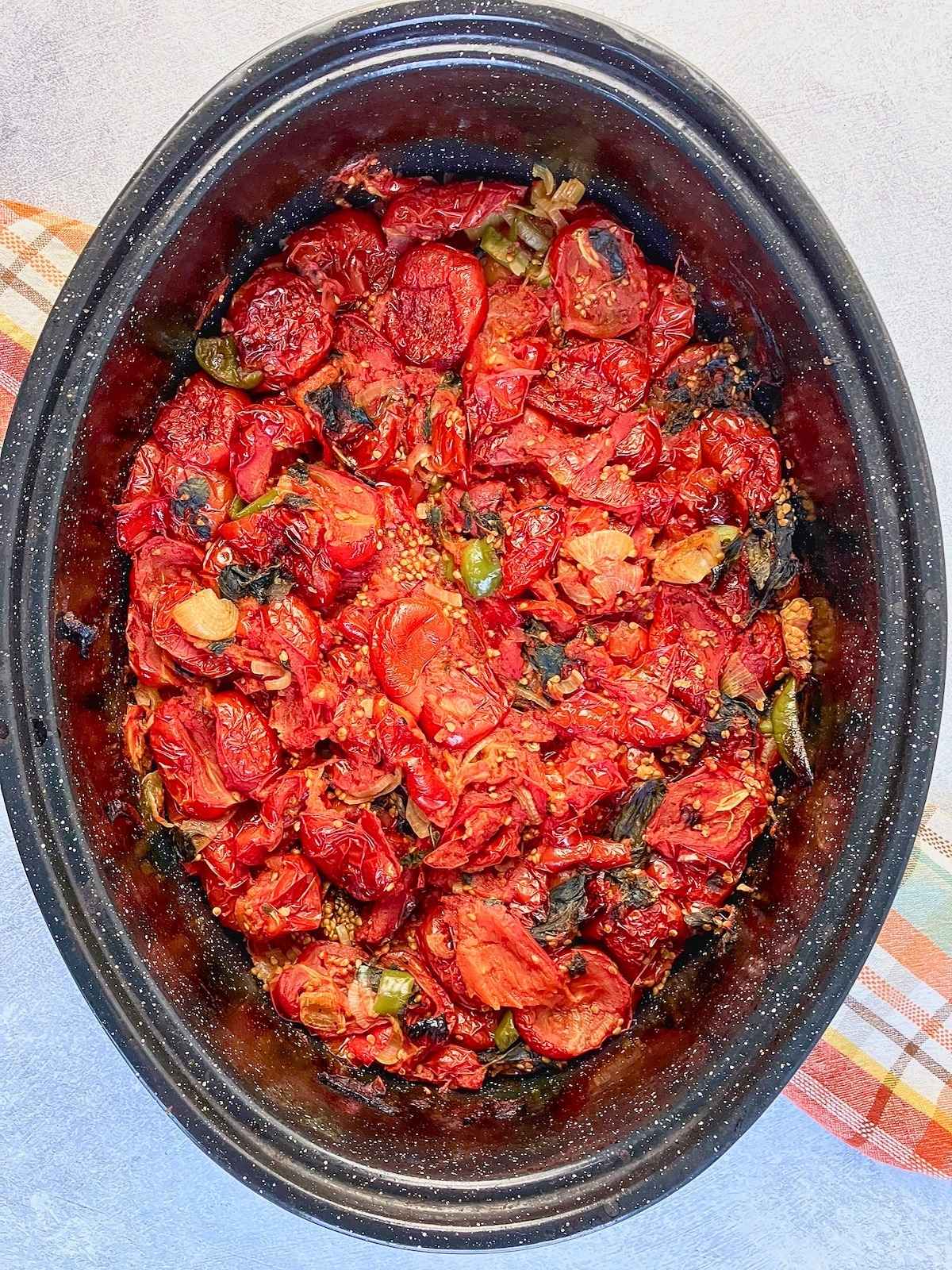 Roasted tomatoes, peppers, onions, and herbs cooked down in a roasting pan with browned edges and concentrated juices. This is the roasted vegetable base before blending into roasted tomato sauce.