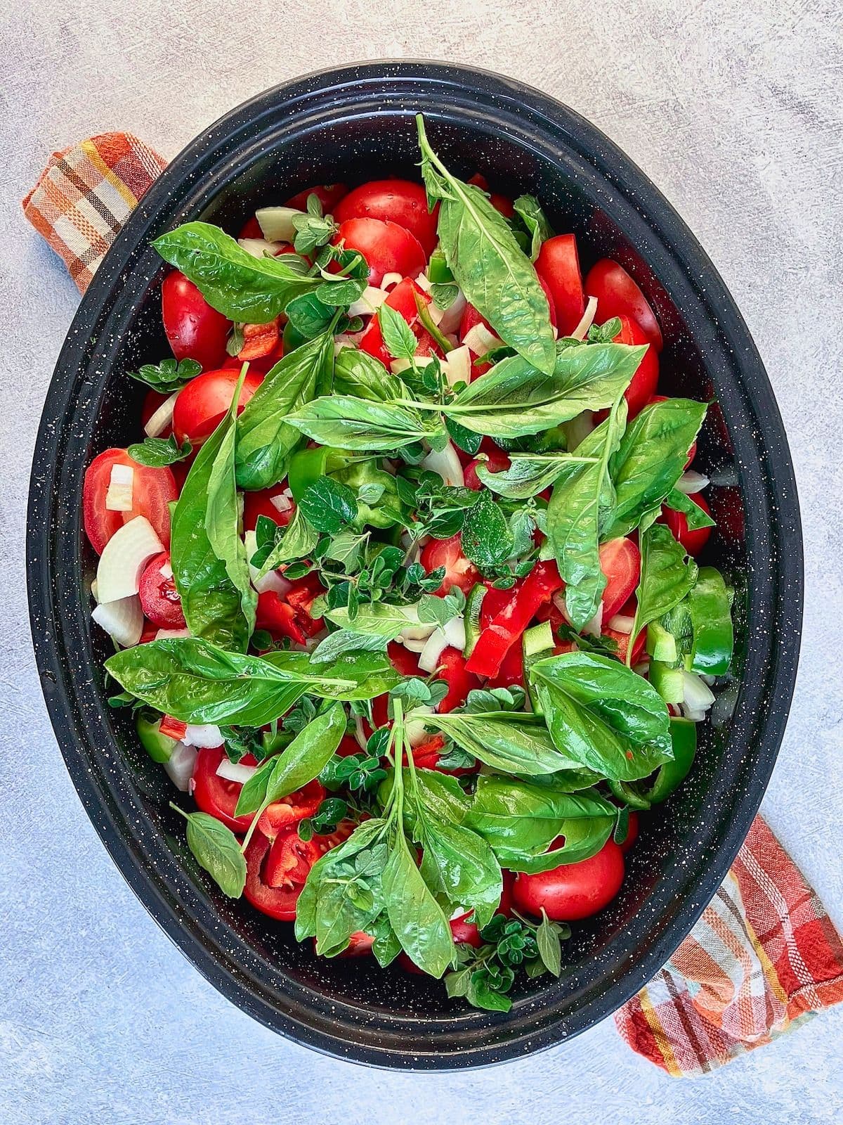 Roasting pan filled with tomatoes, onions, peppers, basil, and fresh herbs before cooking.