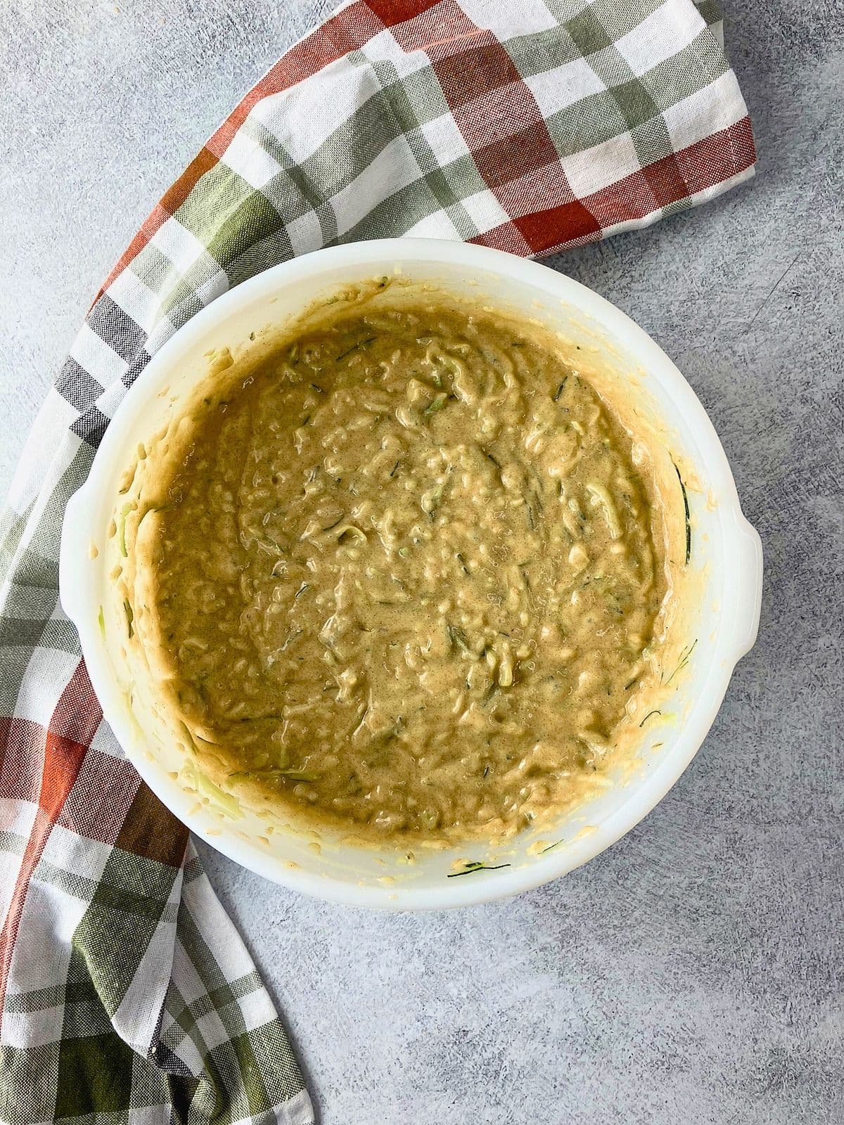 Overhead view of thick apple zucchini bread batter in a white mixing bowl with visible shreds of zucchini throughout.