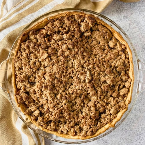Whole apple pie with crumb topping baked in a glass pie dish with a golden crust and an even layer of browned streusel.