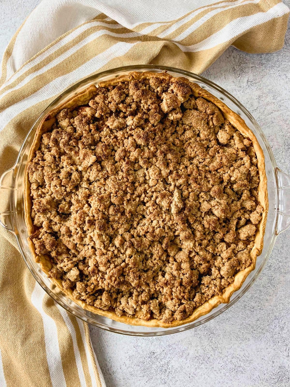 Whole apple pie with crumb topping baked in a glass pie dish with a golden crust and an even layer of browned streusel.
