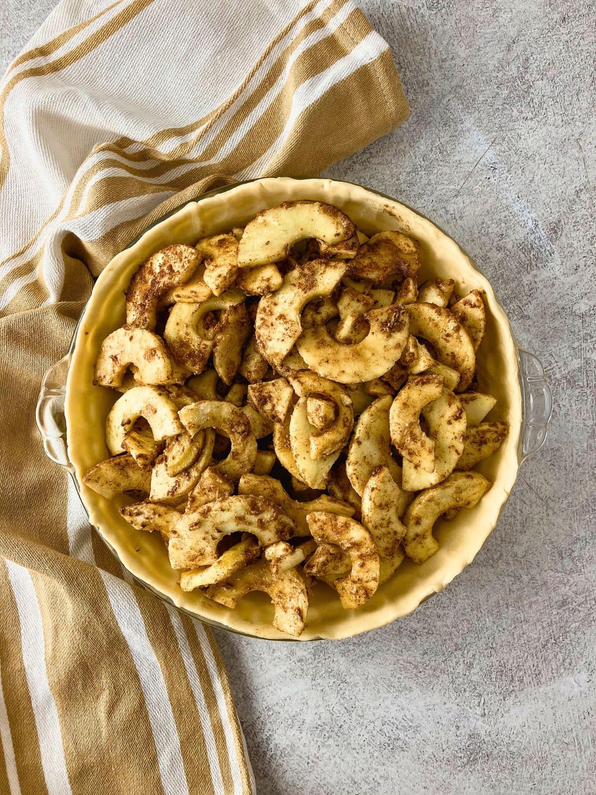 Cinnamon coated apple slices arranged inside an unbaked pie crust in a glass pie dish before adding the crumb topping.