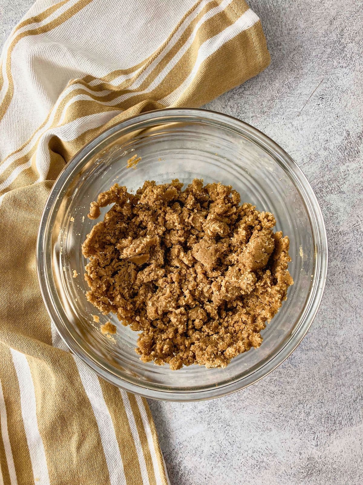 Crumb topping mixture in a clear glass bowl after the dry ingredients have been combined with melted butter.