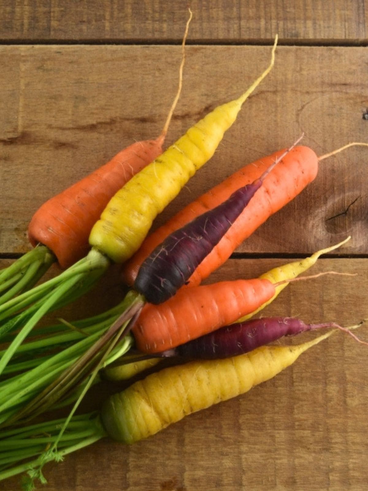 Rainbow carrots just harvested from the garden are lying on a wooden table.