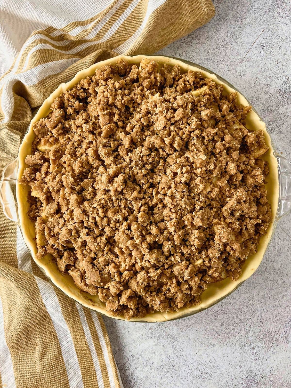 Unbaked apple pie in a glass pie dish covered with a thick crumb topping and ready to go into the oven.