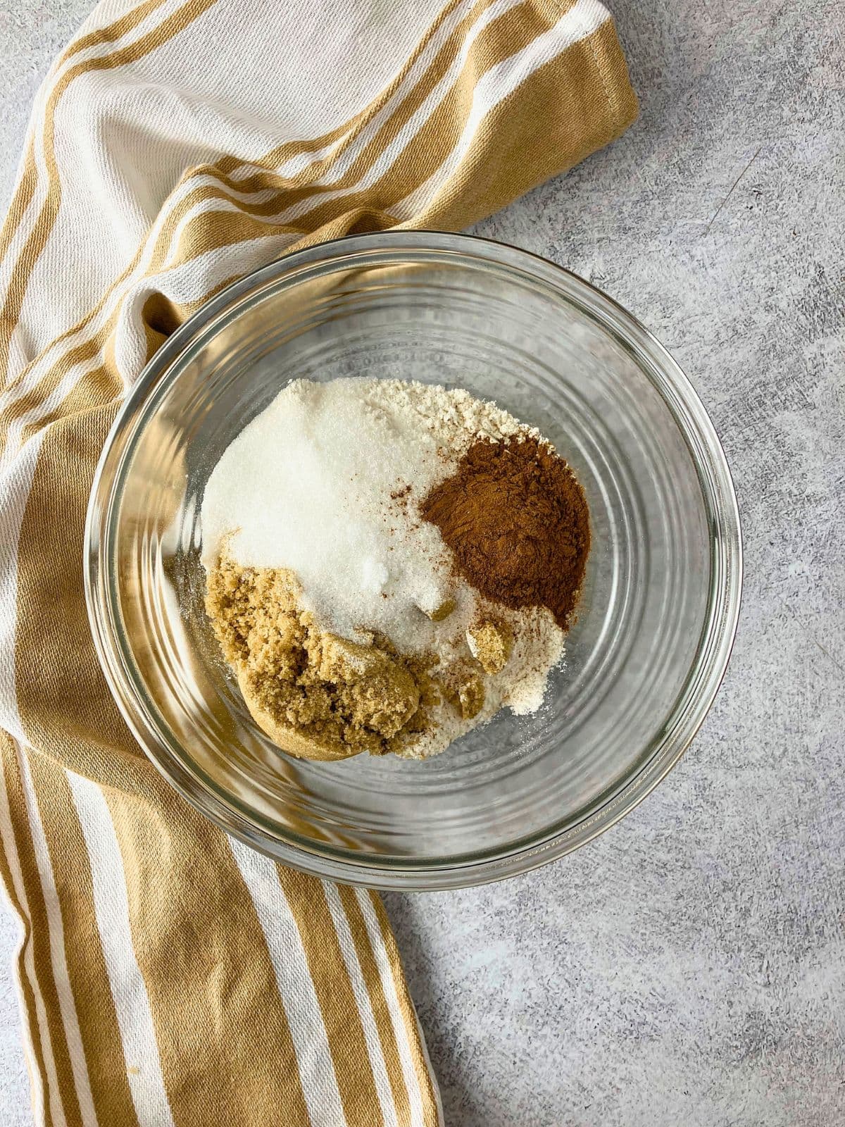 Dry crumb topping ingredients measured into a clear glass bowl including flour white sugar brown sugar and cinnamon before mixing.