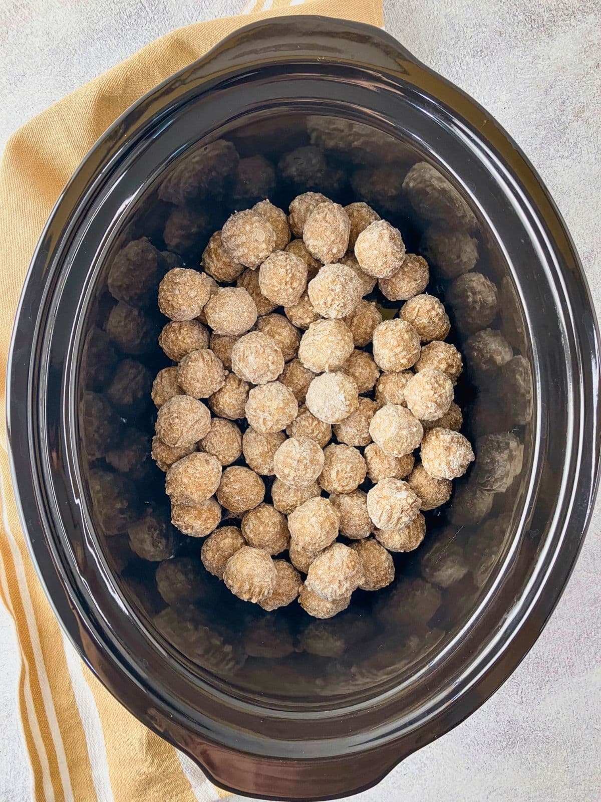 Precooked frozen meatballs arranged in a black slow cooker.