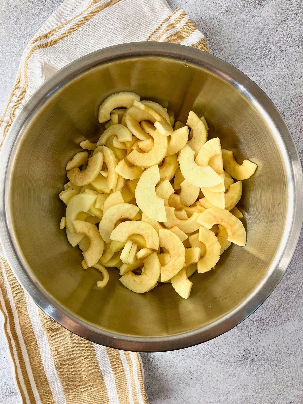 Peeled and sliced apples in a large stainless steel mixing bowl ready to be used for apple pie filling.
