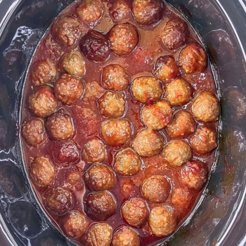Slow cooker meatballs with grape jelly and ketchup inside a black crockpot.
