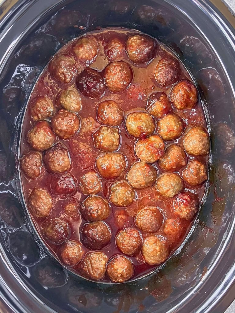 Slow cooker meatballs with grape jelly and ketchup inside a black crockpot.