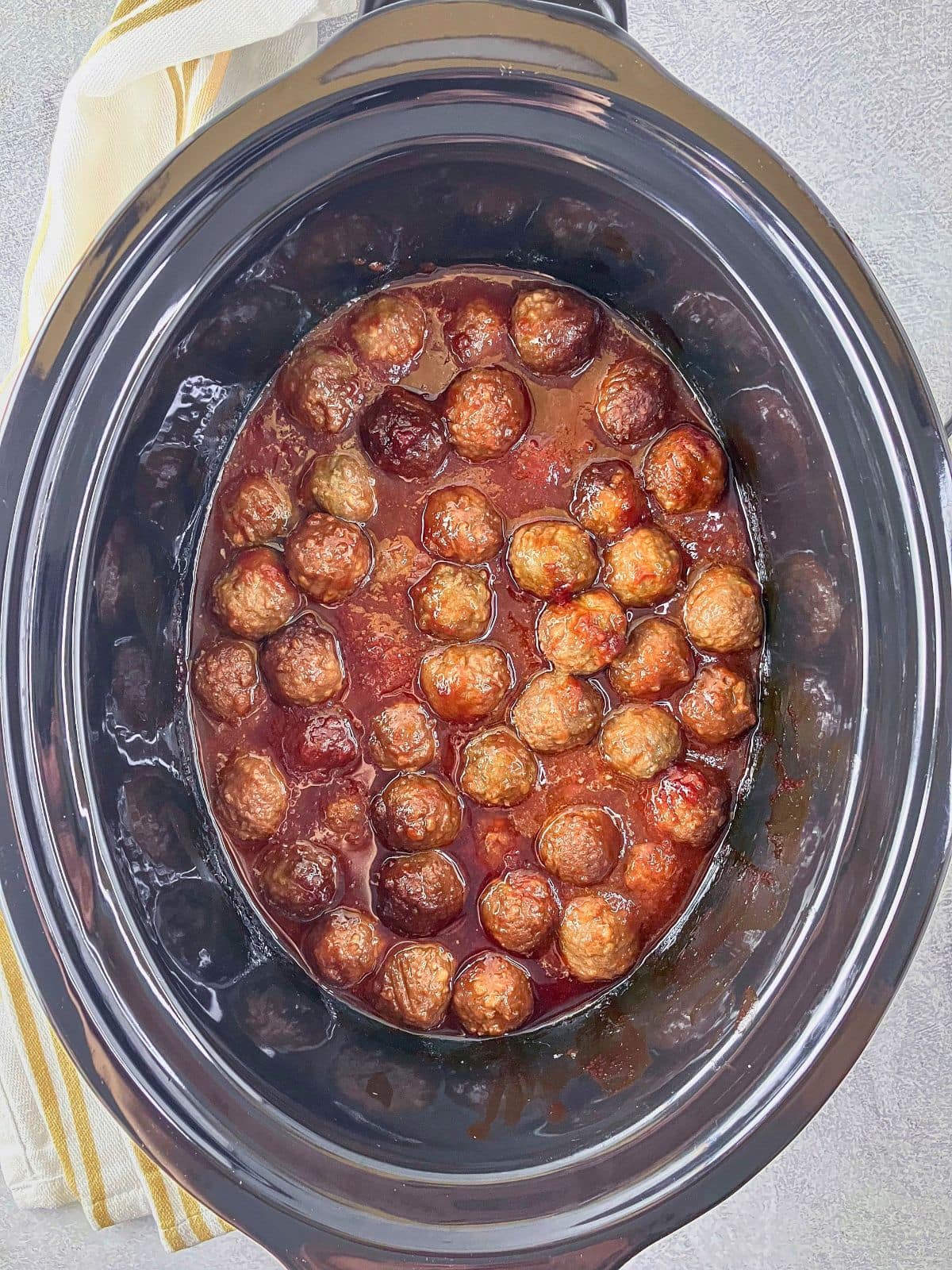 Slow cooker meatballs with grape jelly and ketchup simmering inside a black crockpot.