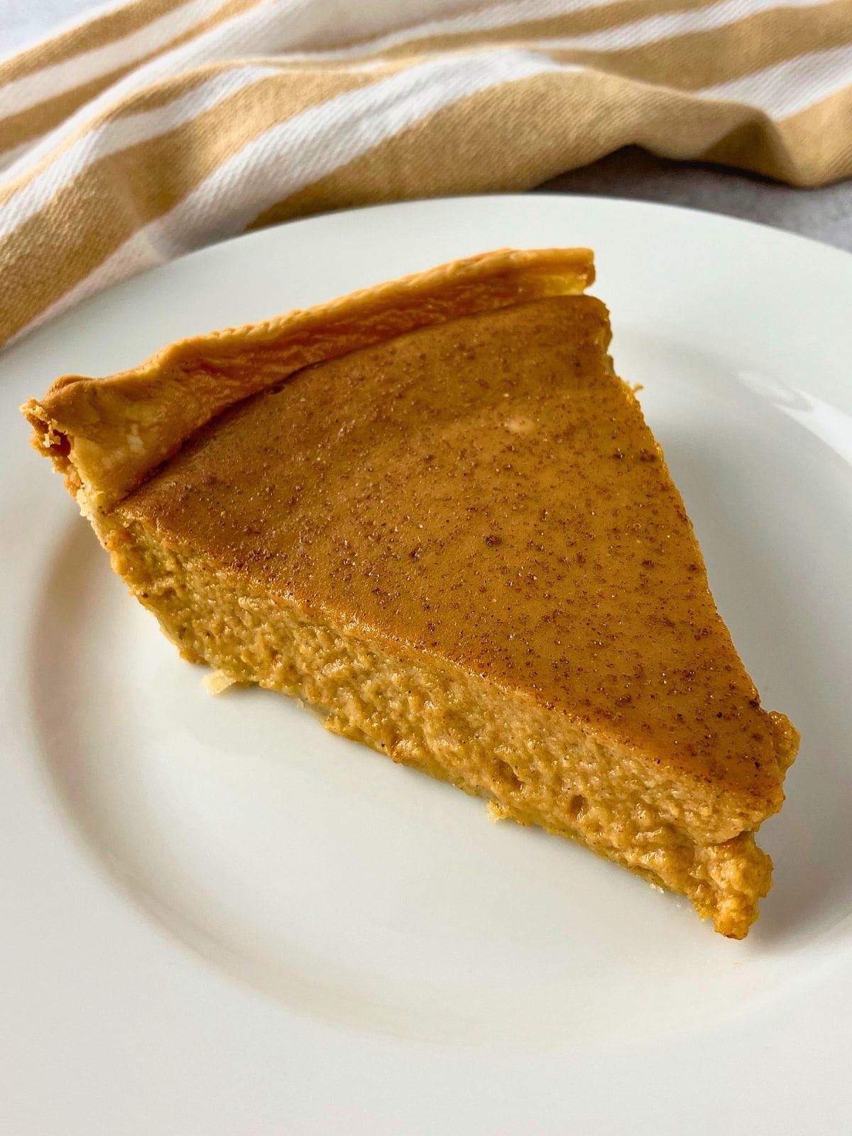 Close up slice of pumpkin pie without evaporated milk on a white plate with a creamy spiced filling and crisp golden crust.