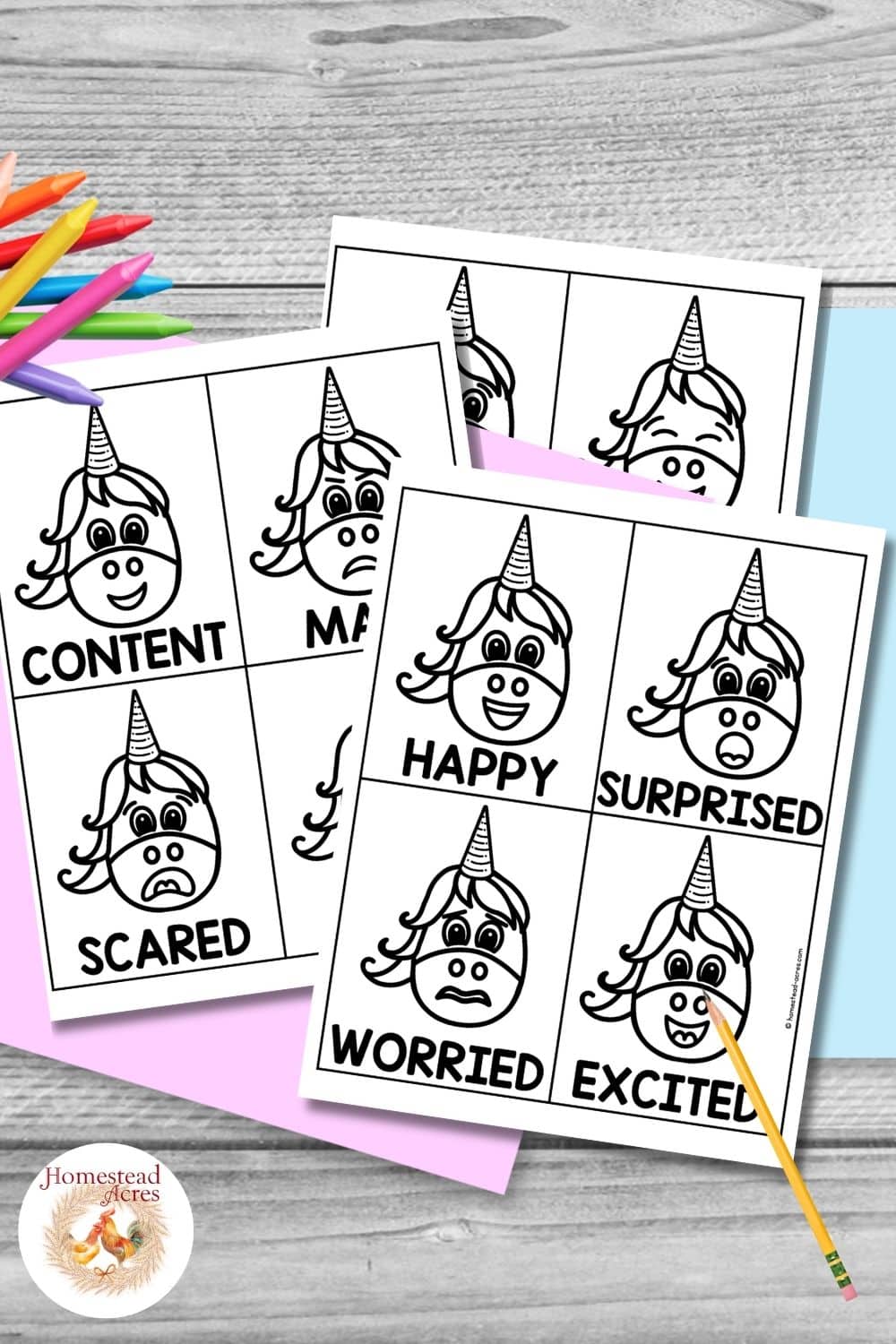 Black and white unicorn emotion cards arranged on pastel paper with colorful crayons and a pencil on a gray wood background. Visible feeling labels include "CONTENT". "MAD". "SCARED". "HAPPY". "SURPRISED". "WORRIED". "EXCITED".